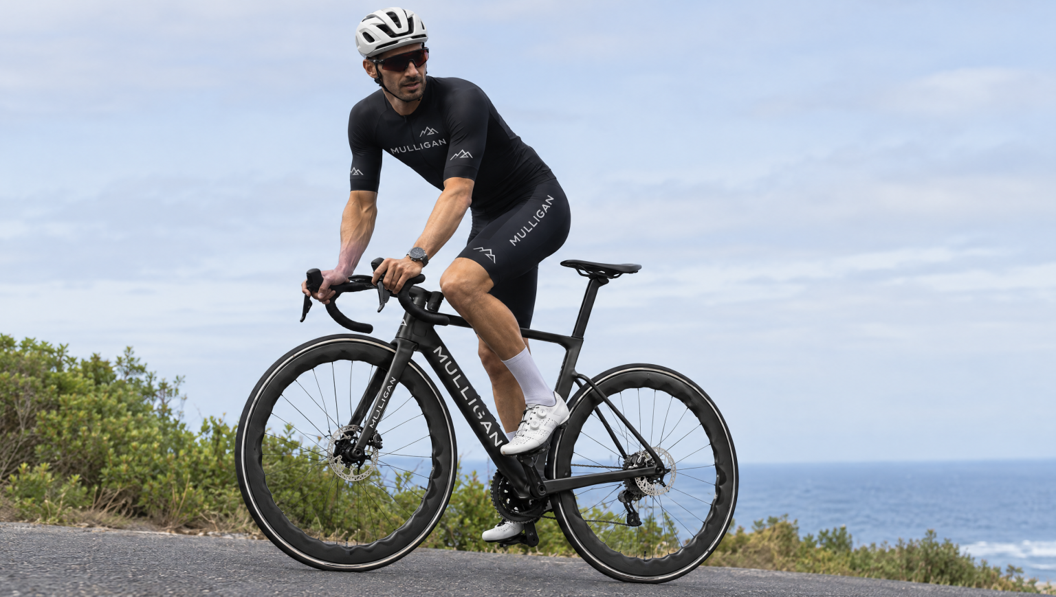 Cycliste en tenue MULLIGAN sur le vélo de route carbone R15 PRO face à la mer